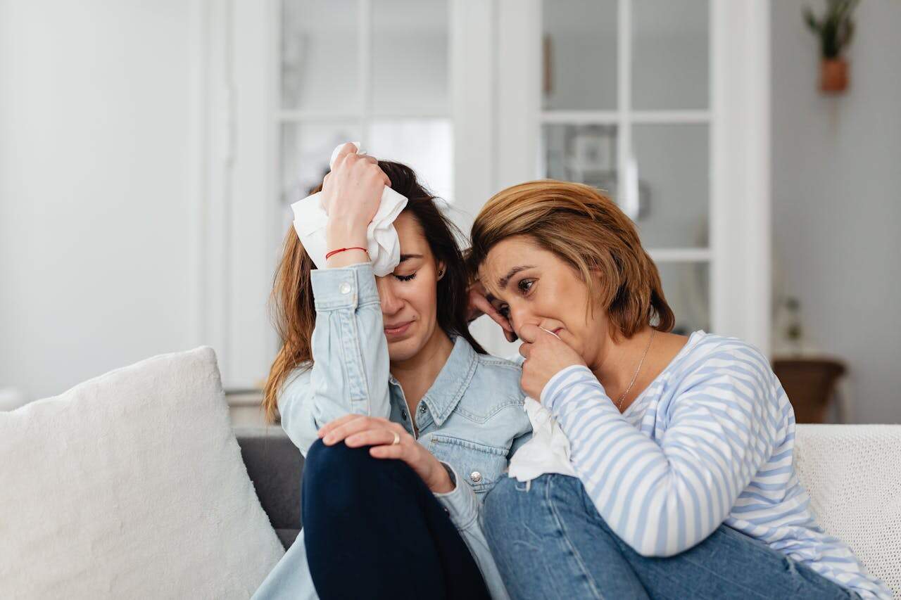 Two women sitting on a sofa, comforting each other in a moment of shared emotions.